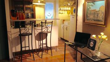 Une cuisine chaleureuse avec un coin bar, deux tabourets de bar, une table à plateau en verre ornée d’un vase de fleurs et un tableau encadré accroché au mur.