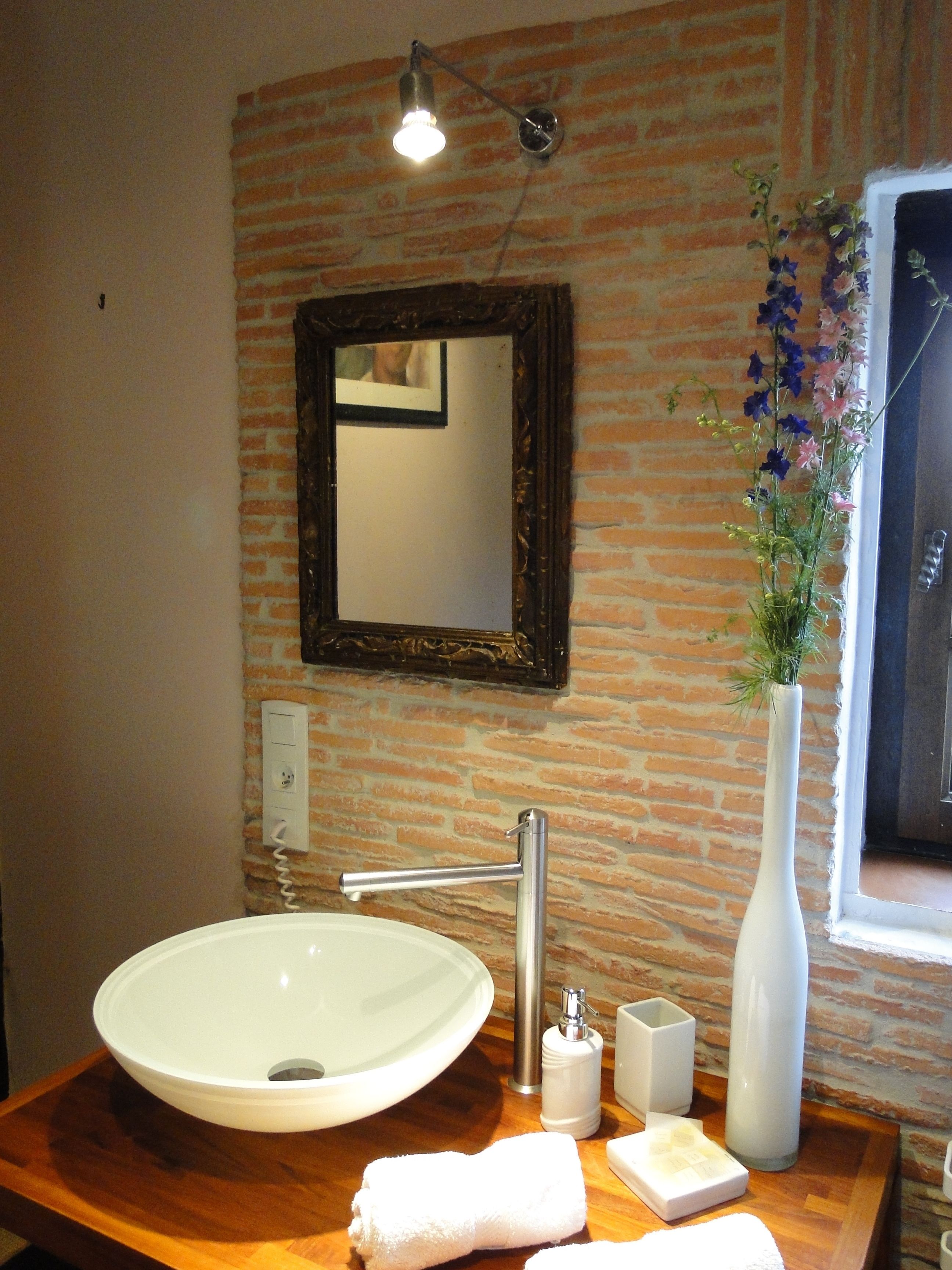A bathroom with a white sink, a mirror, a vase with flowers, and a wooden countertop.