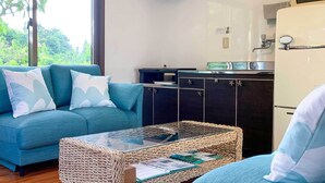 A living room with a sofa, a glass-top coffee table, and a kitchen area with cabinets and a refrigerator.