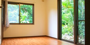 A room with a large window, wooden flooring, and a view of a lush garden. - Ishigakijima Cottage Kachibai (Ishigaki)