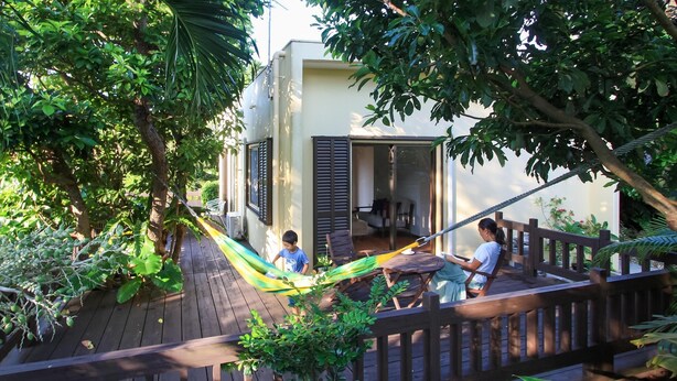 A wooden deck with a hammock, a wooden fence, and lush greenery.