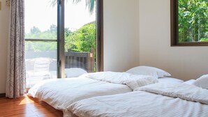 A bedroom with a large bed, a sliding glass door leading to a balcony, and a view of greenery outside.