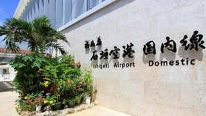 A sign for Ishigaki Airport Domestic with a stone wall and potted plants.