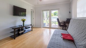 Un salon équipé d’un téléviseur à écran plat, d’un ventilateur de plafond, d’un canapé et d’une porte-fenêtre coulissante donnant sur une terrasse extérieure.