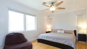 Une chambre avec un lit, un ventilateur de plafond, une fenêtre et un fauteuil en forme de sac de haricots.