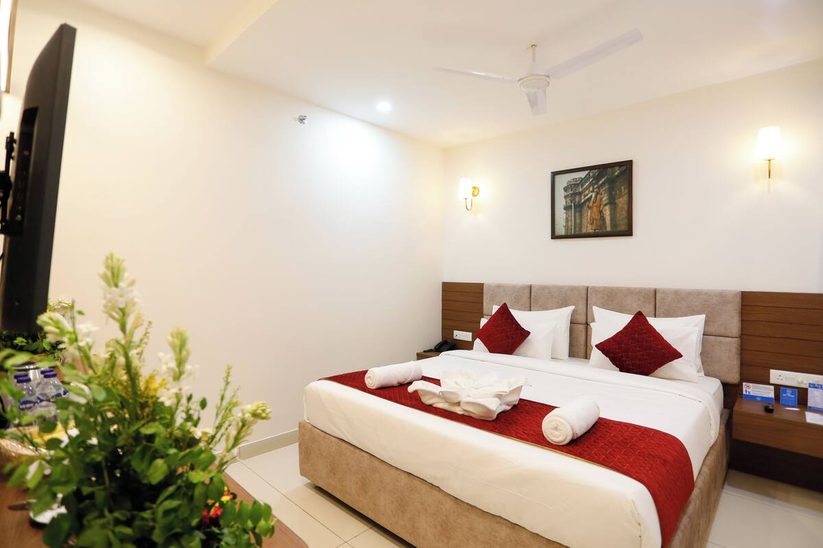 Una habitación de hotel con una cama grande, un ventilador de techo, una mesita de noche y una lámpara de pared.