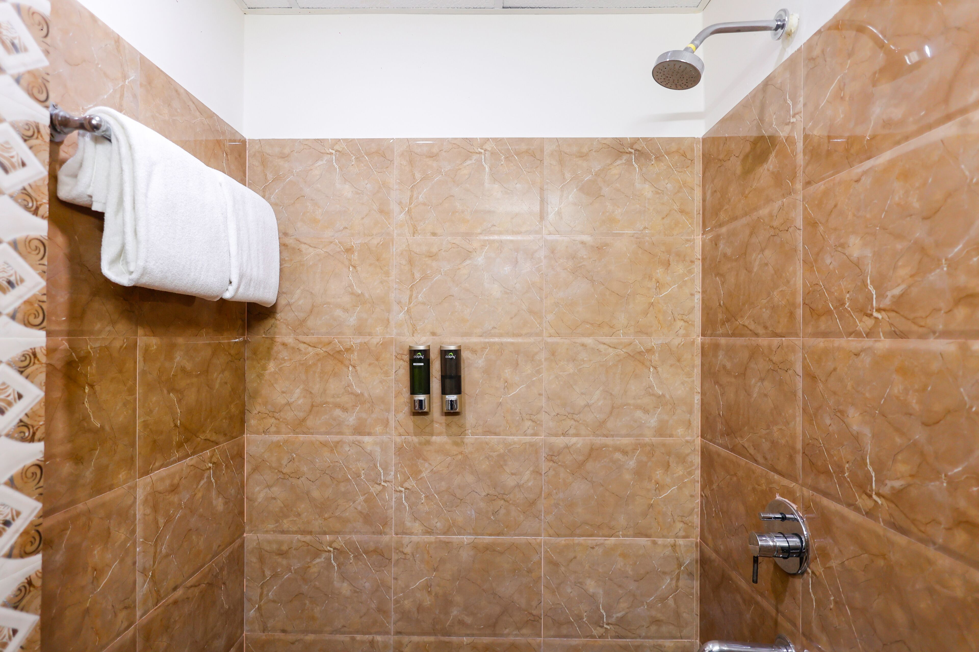 Une salle de bain carrelée de marbre, avec un porte-serviettes, deux articles de toilette et une pomme de douche.