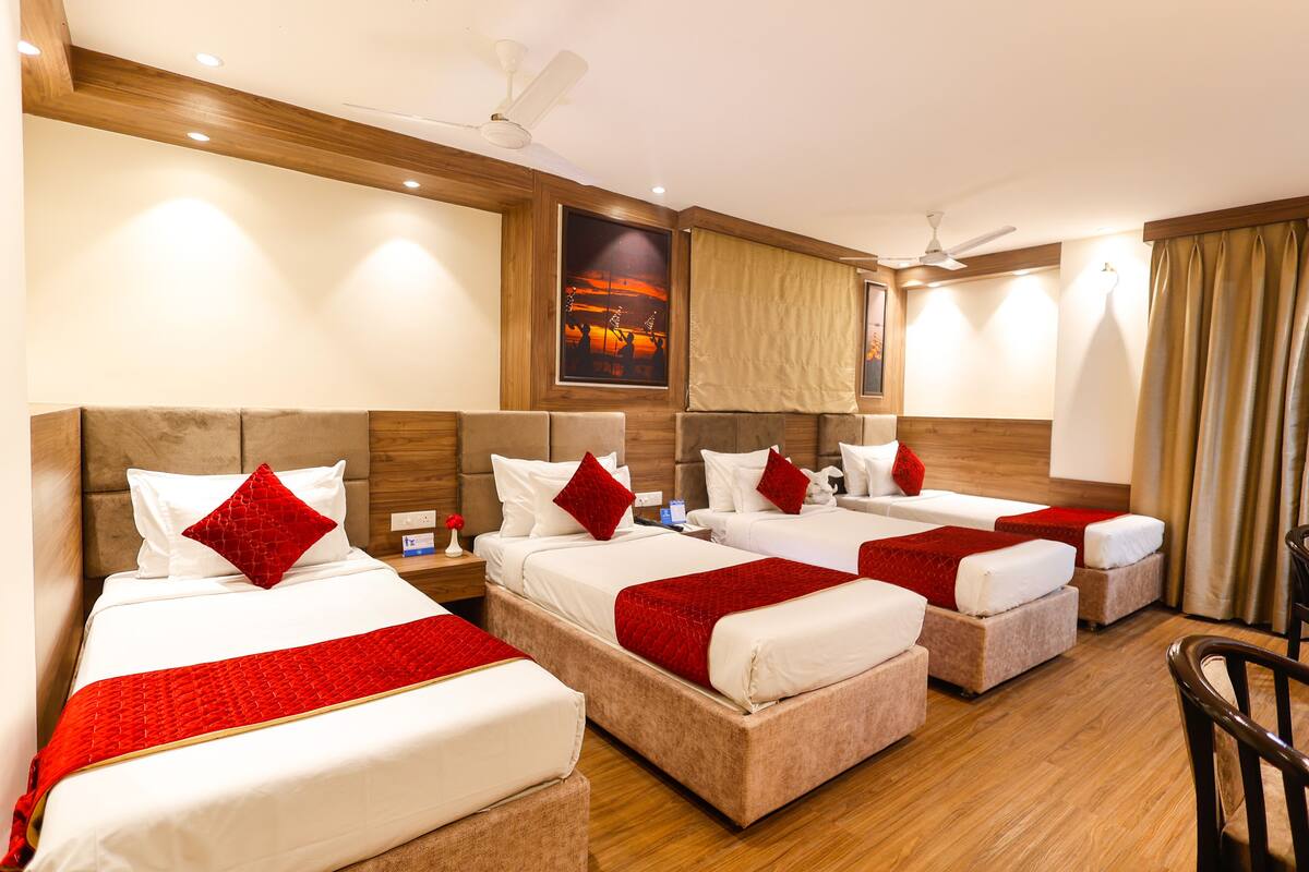 Habitación de hotel con cuatro camas, cada una con ropa de cama blanca y detalles en rojo, cabeceros de madera y un cuadro grande en la pared.
