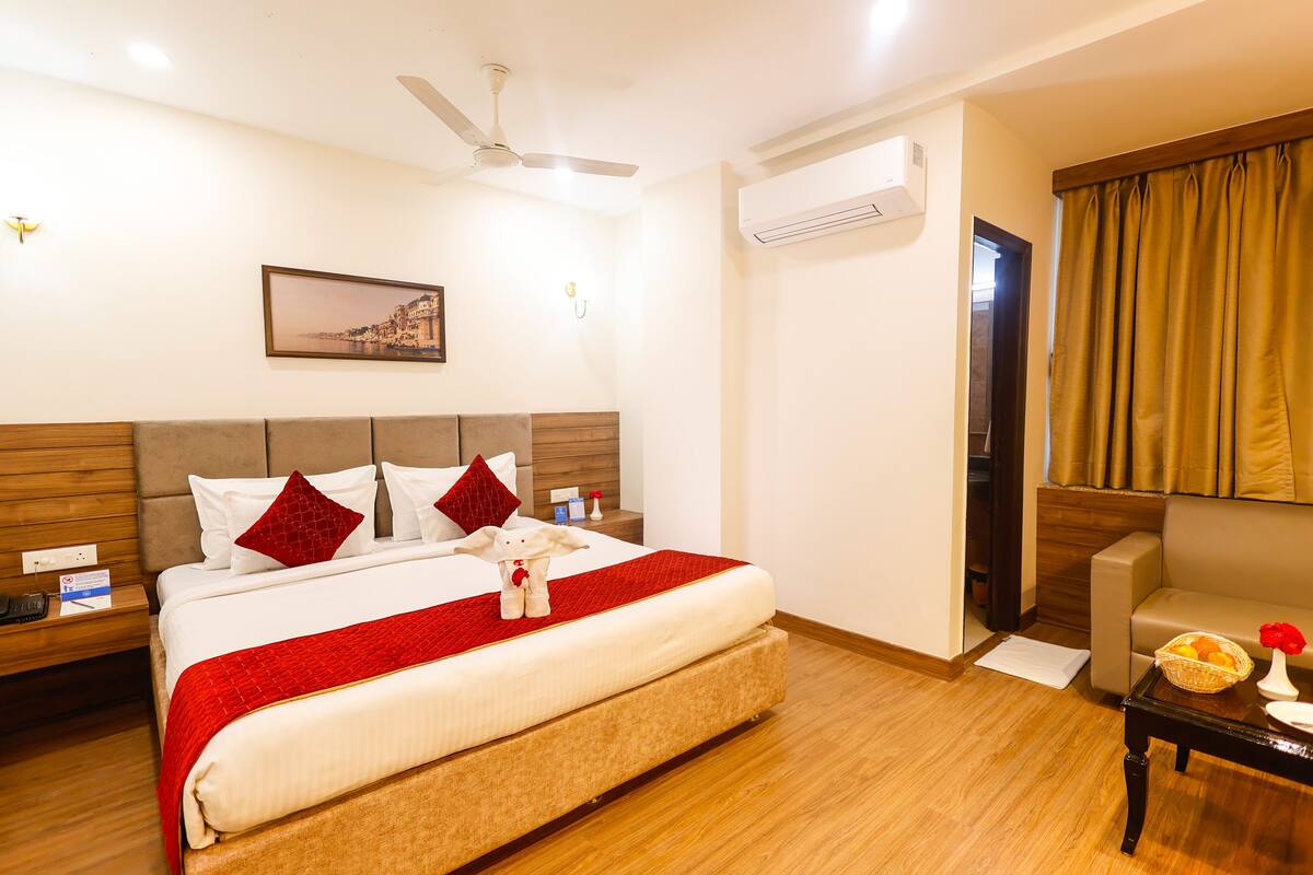 Habitación de hotel con cama, mesita de noche, escritorio, silla, ventilador de techo, aire acondicionado y ventana con cortinas.