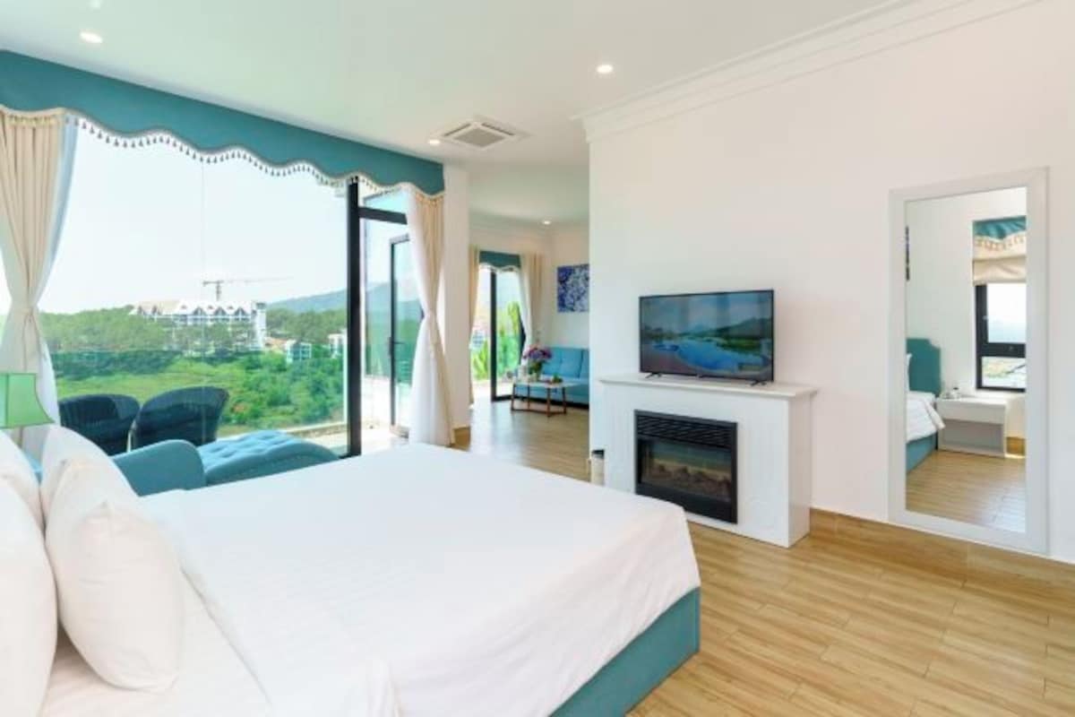 Una habitación de hotel moderna con una cama grande, televisión, chimenea y balcón con vistas panorámicas.