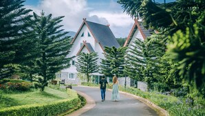 A couple walking on a road towards a house with a steep roof and wooden beams. - Dalat Wonder Resort (Xuan Huong - Da Lat)