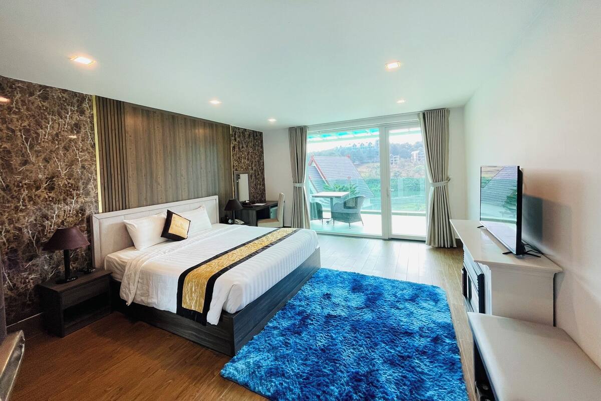 Ein modernes Hotelzimmer mit einem großen Bett, einem Schreibtisch, einem Fernseher und einem Balkon mit Blick.