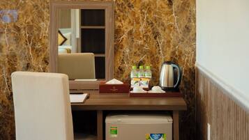 Quarto de hotel compacto com parede de mármore, pequena escrivaninha com espelho, cadeira, minibar e frigorífico.