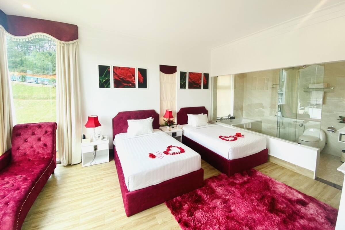 Ein Hotelzimmer mit zwei Betten, einem großen Spiegel, einer Dusche und Blick auf Grünflächen.