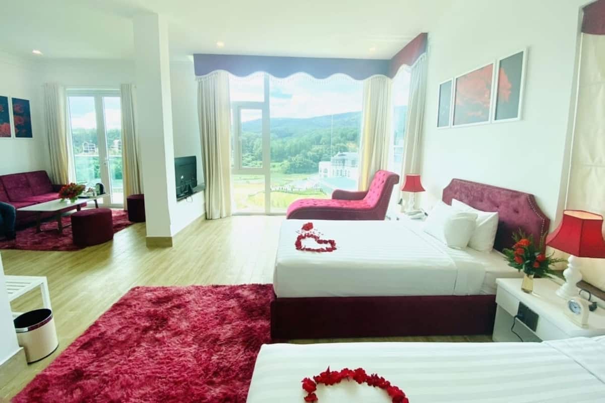 Une chambre d’hôtel avec un lit, un canapé, une télévision, une fenêtre donnant sur un beau paysage et un tapis rouge.