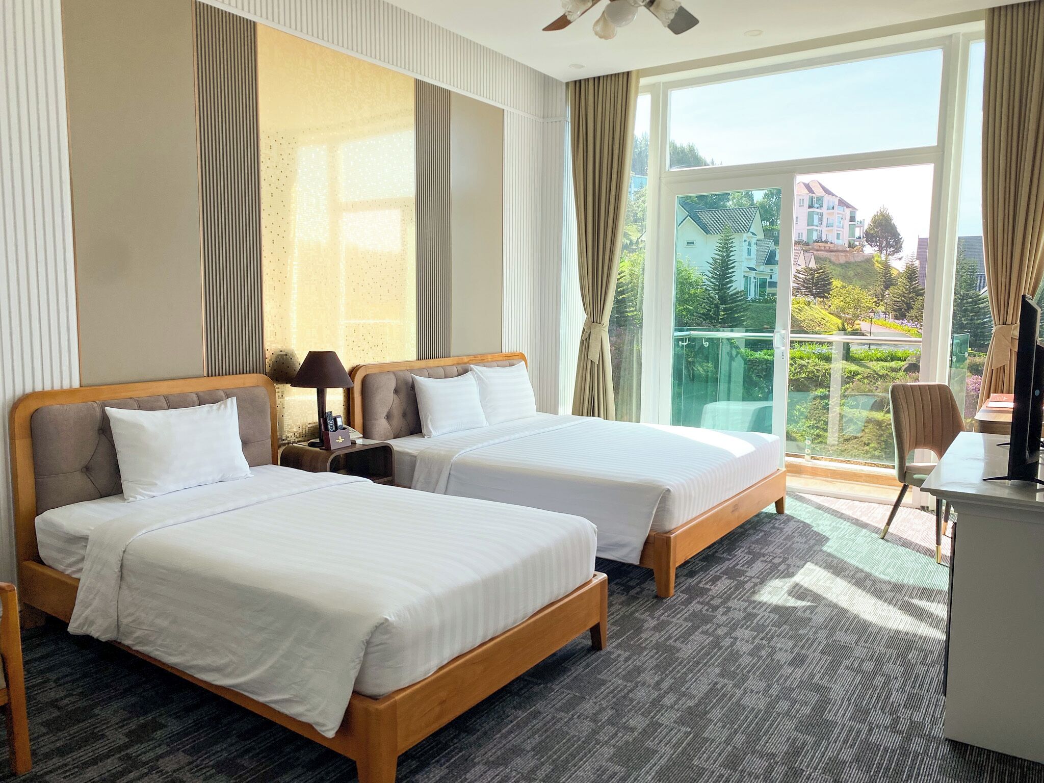 Habitación de hotel con dos camas, un escritorio, una silla y un amplio ventanal con vistas al exterior.