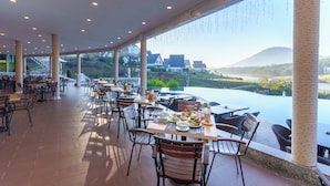 A restaurant with outdoor seating overlooking a scenic view of a lake and mountains. - Dalat Wonder Resort (Xuan Huong - Da Lat)