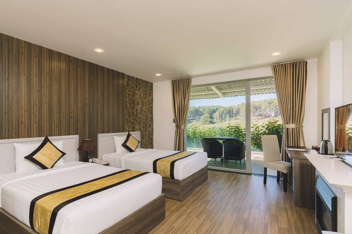 Ein Hotelzimmer mit zwei Betten, einem Schreibtisch und Blick auf Grünflächen.