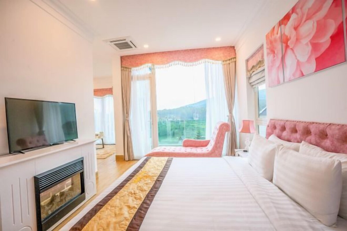 A bedroom with a bed, a television, a fireplace, and a view of the outdoors.