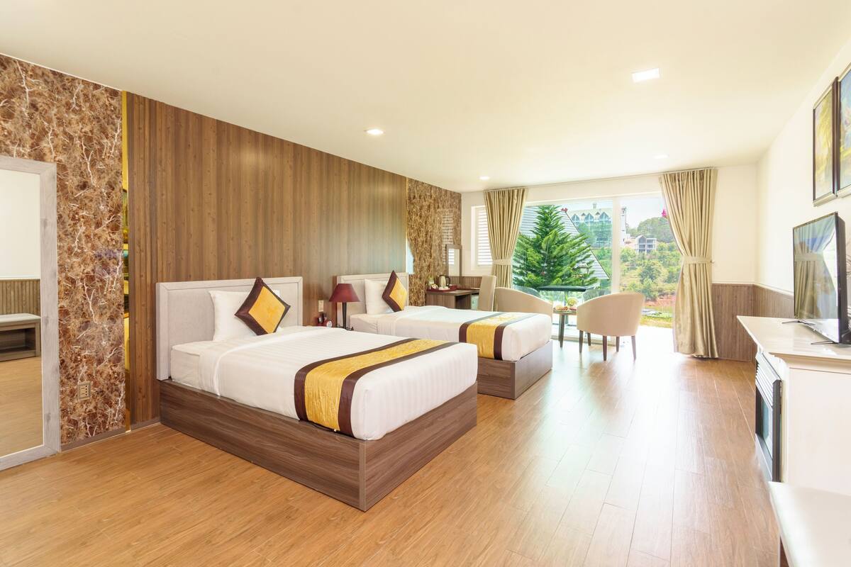 Ein Hotelzimmer mit zwei Betten, einem Schreibtisch, einem Stuhl und Blick auf Grünflächen.
