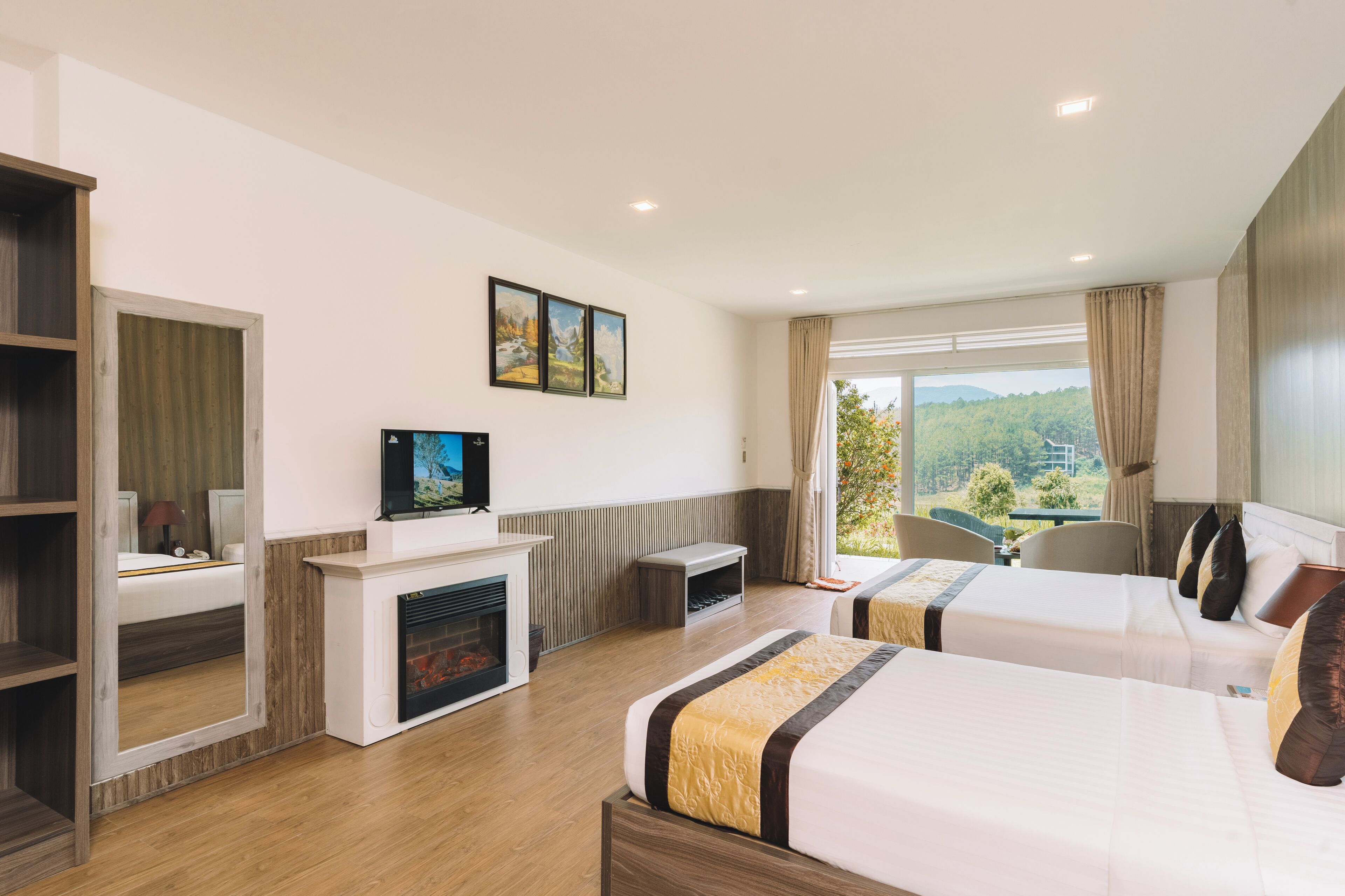 Habitación de hotel con dos camas, chimenea, televisión y un amplio ventanal con vistas a zonas verdes.