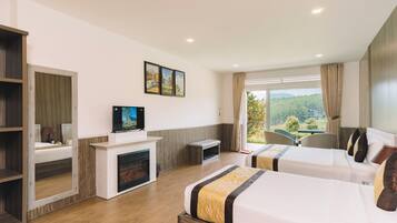 Habitación de hotel con dos camas, chimenea, televisión y un amplio ventanal con vistas a zonas verdes.