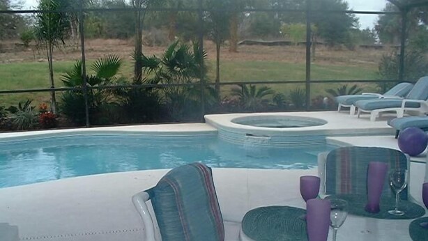 A poolside area with lounge chairs and a table set for dining, surrounded by a fence and greenery. - Ly53766 - Indian Ridge - 4 Bed 2 Baths Villa (Kissimmee)