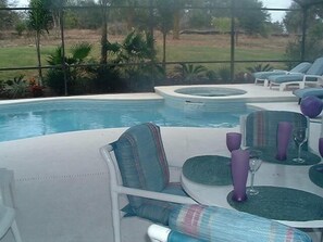 A poolside area with lounge chairs and a table set for dining, surrounded by a fence and greenery. - Ly53766 - Indian Ridge - 4 Bed 2 Baths Villa (Kissimmee)