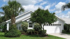 A single-story house with a white exterior, a garage, and a well-maintained lawn with various shrubs and a palm tree. - Ly53766 - Indian Ridge - 4 Bed 2 Baths Villa (Kissimmee)
