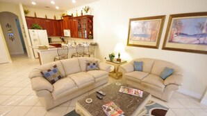 A living room with two beige sofas, a coffee table, and a kitchen in the background. - Ly53766 - Indian Ridge - 4 Bed 2 Baths Villa (Kissimmee)