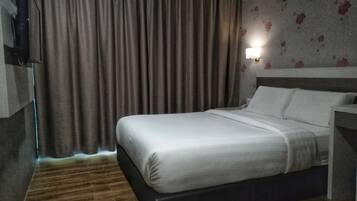 A hotel room with a large bed, wooden flooring, a TV mounted on the wall, and a floral wallpaper pattern.