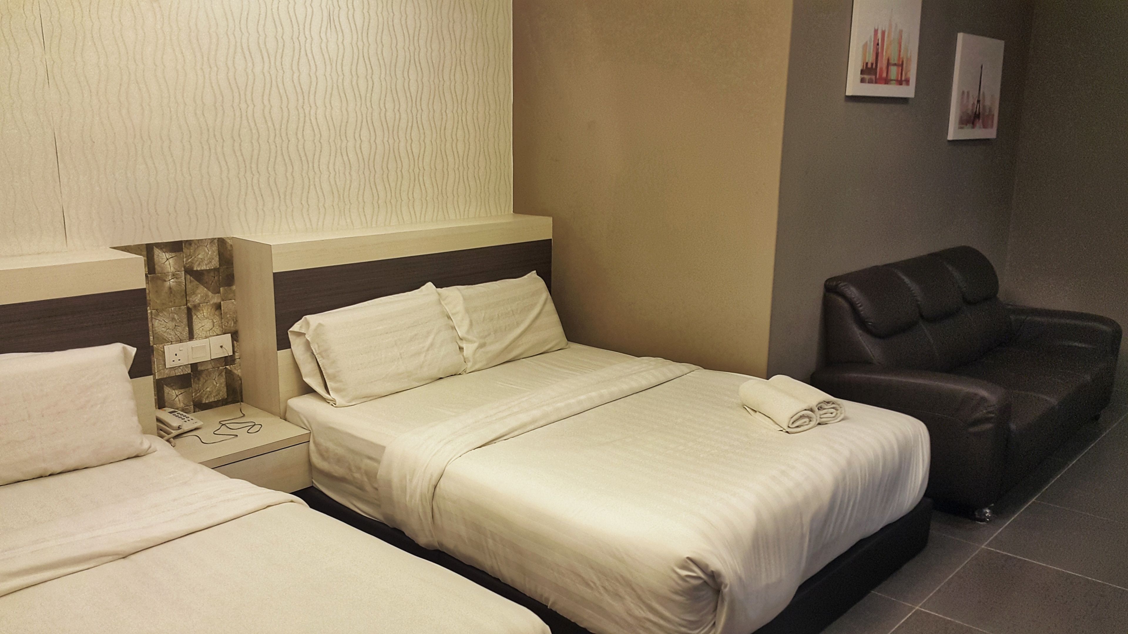 A hotel room with two beds, a nightstand, a telephone, and a leather armchair.