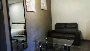Una habitación moderna con un espejo grande, una mesa de centro de vidrio, un sofá de cuero negro y dos cuadros enmarcados en la pared.