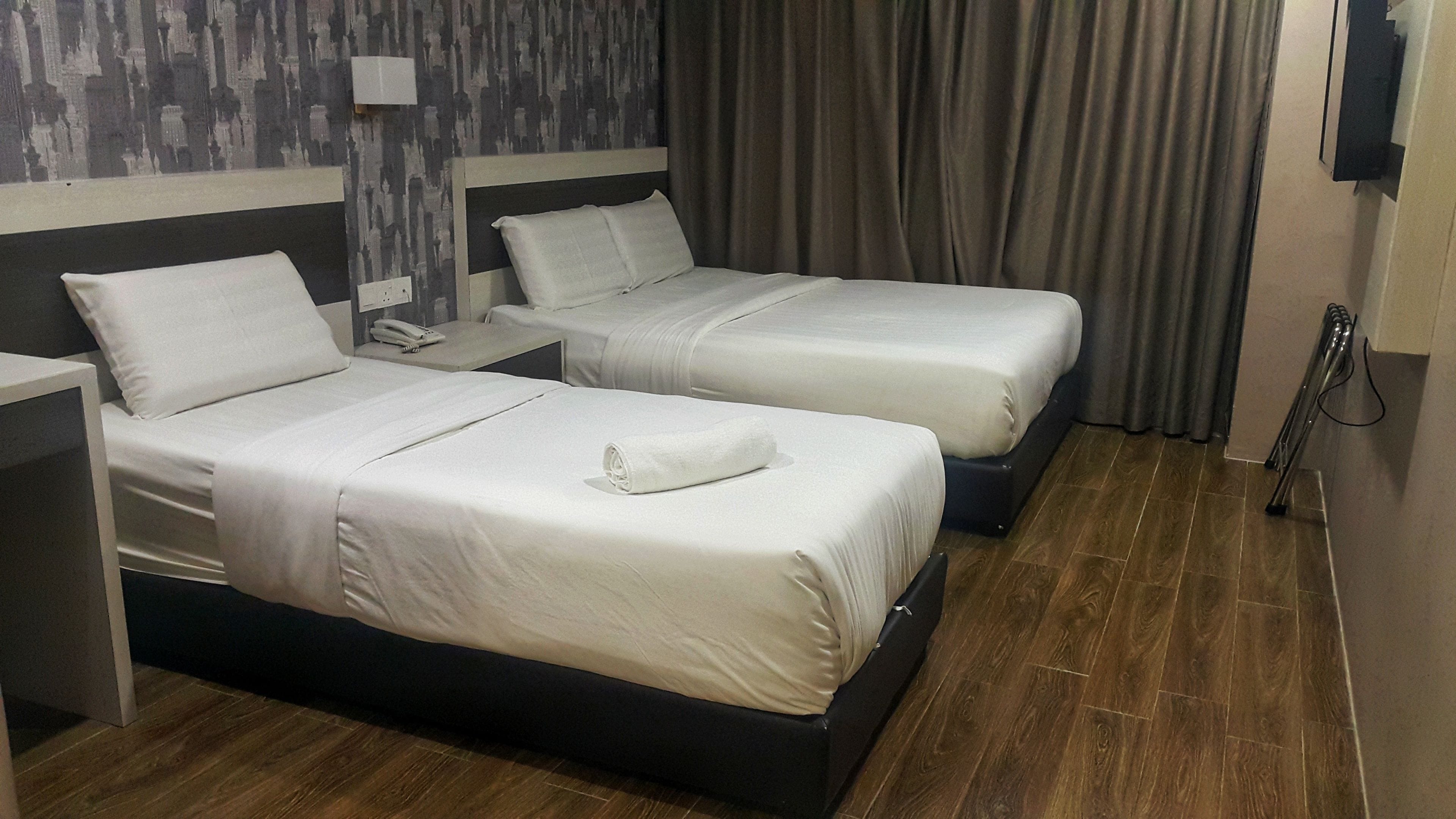 Een hotelkamer met twee bedden, een nachtkastje met een telefoon, een wandlamp en een gordijn.