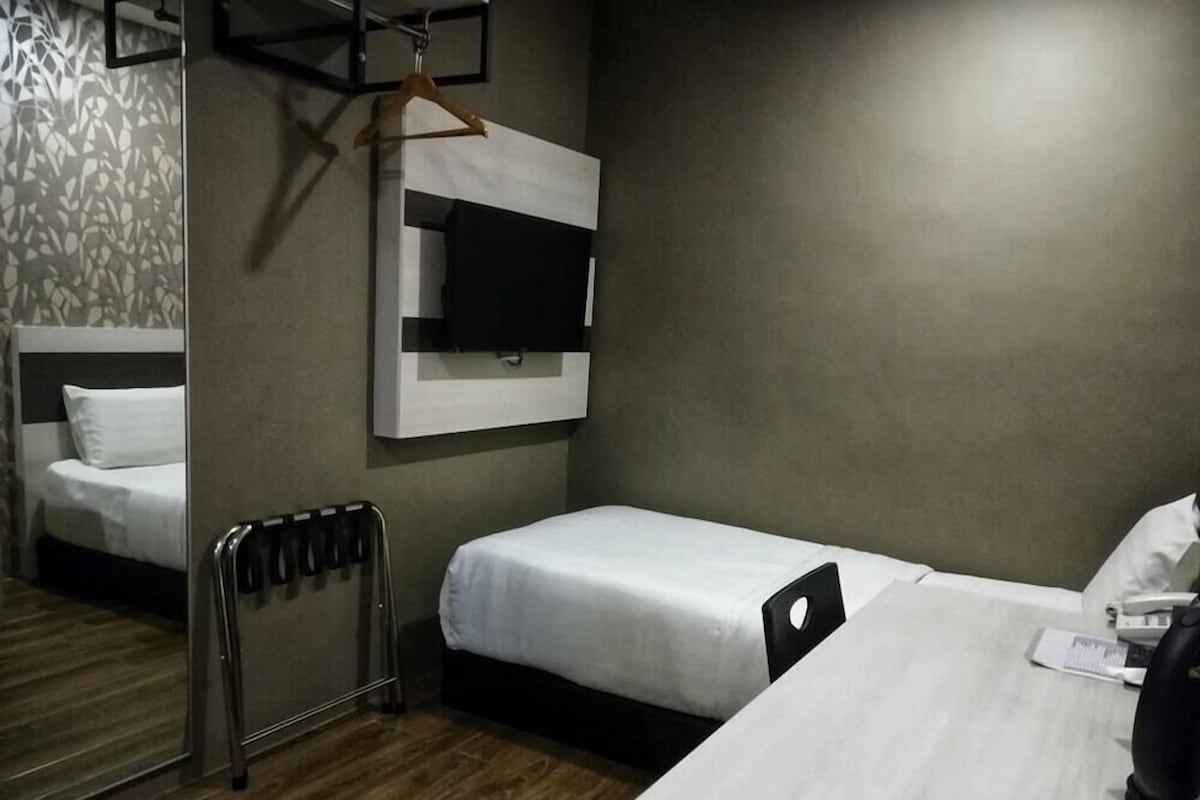 Una habitación de hotel con dos camas, un escritorio, un televisor montado en la pared y un radiador.