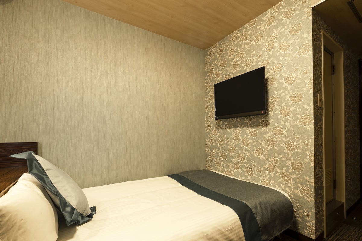 A hotel room with a bed, a TV mounted on the wall, and a door leading to another room.