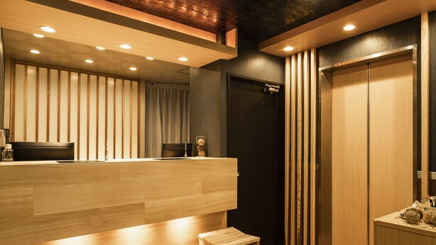 Una zona de recepción moderna con un mostrador de madera, un taburete de madera pequeño y una puerta de ascensor negra.