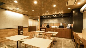 Un restaurante con mesas y sillas de madera, una zona de cocina y un techo con diseño.