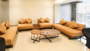 Un salon moderne avec un canapé d’angle, deux tables basses et une fenêtre à motifs.