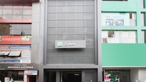 La façade d’un immeuble porte une enseigne indiquant « Elite Residency », et divers commerces sont installés au rez-de-chaussée.