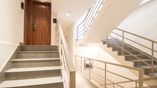 Un escalier avec une porte en bois en haut, une main courante et un mur de couleur claire.