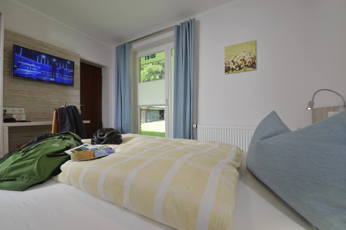 Une chambre d’hôtel avec un lit, un téléviseur fixé au mur, une fenêtre avec des rideaux et un radiateur.