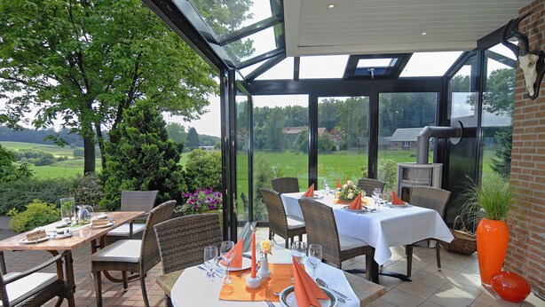 Une véranda dotée d’un toit en verre, avec des tables et des chaises pour les repas.
