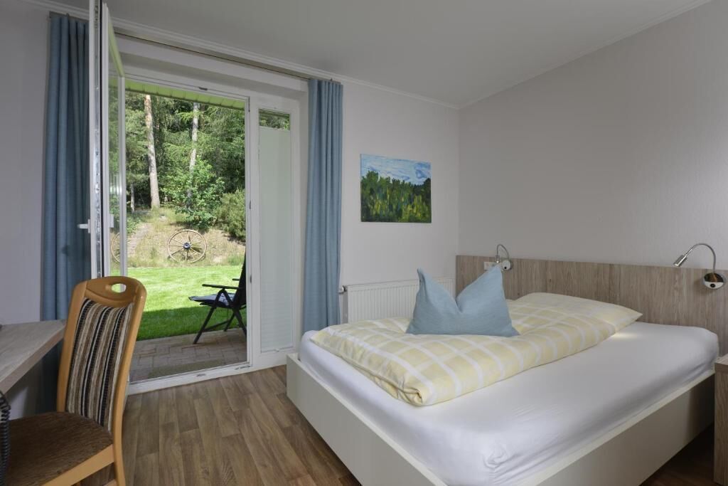 A bedroom with a bed, a chair, a table, and a view of the outdoors through a sliding door.