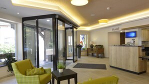 Un hall d’hôtel comprenant un comptoir d’accueil, un espace salon et une porte vitrée donnant sur un espace extérieur.