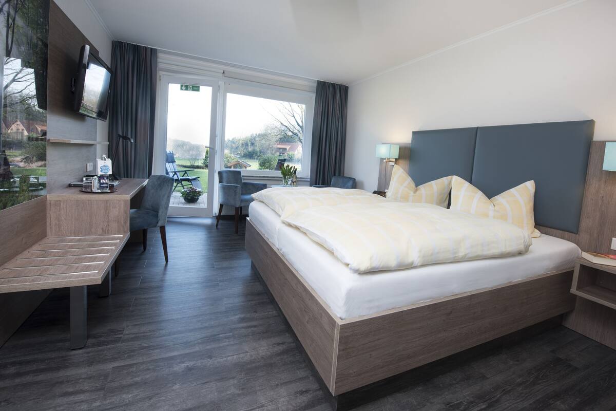 Une chambre d’hôtel avec un grand lit, un bureau avec une chaise, un téléviseur fixé au mur et une vue sur l’extérieur.