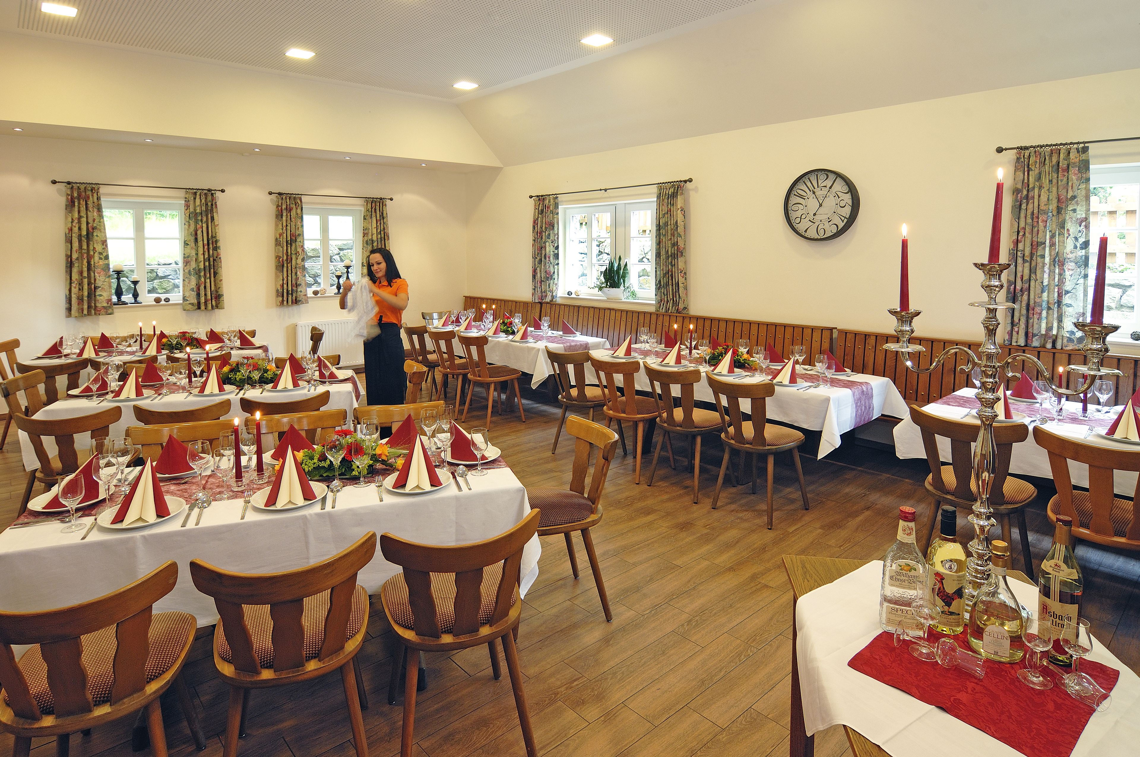 A dining area with multiple tables set for a meal, wooden chairs, and a clock on the wall.
