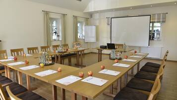 A conference room with long tables, chairs, a projector screen, and a whiteboard.