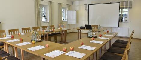 A conference room with long tables, chairs, a projector screen, and a whiteboard.