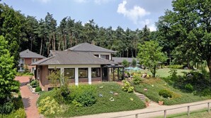 Il s’agit d’une propriété résidentielle comprenant une maison principale et une dépendance plus petite attenante, le tout entouré d’une végétation luxuriante et d’un jardin bien entretenu.